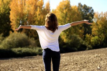 Junge Frau mit ausgestreckten Armen im Park schaut in die Sonne