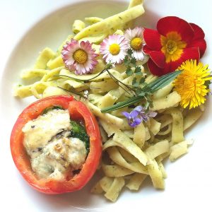 Teller mit Kräuternudeln, mit Wildkräutern gefüllte, überbackene Tomate, Wildblumen als Deko