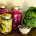 Drei Gläser mit fermentiertem Gemüse, eine schale Salz und ein Wirsingkopf
